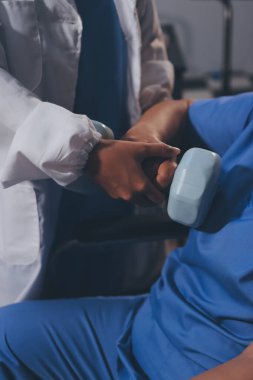 Evde dambıl kullanarak fizyoterapist eğitimi alan yaşlı bir kadın. Terapist, huzurevi egzersizlerinde yaşlı kadına yardım ediyor. Yaşlı bir hasta kollarını uzatmış halterler kullanıyor..