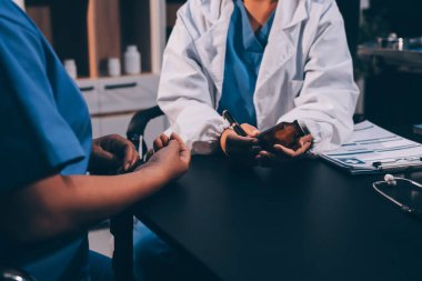 Evde dizüstü bilgisayar kullanan yaşlı kadın hemşireyle birlikte ilaç şişesini tutuyor.