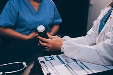 Evde dizüstü bilgisayar kullanan yaşlı kadın hemşireyle birlikte ilaç şişesini tutuyor.