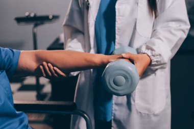 Evde dambıl kullanarak fizyoterapist eğitimi alan yaşlı bir kadın. Terapist, huzurevi egzersizlerinde yaşlı kadına yardım ediyor. Yaşlı bir hasta kollarını uzatmış halterler kullanıyor..