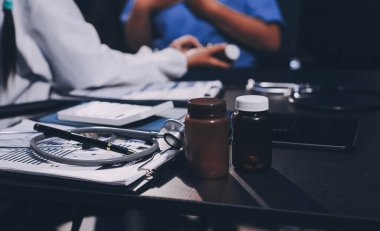 Evde dizüstü bilgisayar kullanan yaşlı kadın hemşireyle birlikte ilaç şişesini tutuyor.