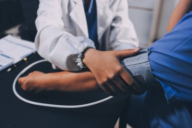 Hastanın tansiyonunu ölçen bir doktor. Hastanın kolunda tansiyon aleti var. Doktor da tansiyon monitörü kullanıyor..