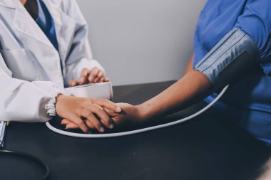 Hastanın tansiyonunu ölçen bir doktor. Hastanın kolunda tansiyon aleti var. Doktor da tansiyon monitörü kullanıyor..