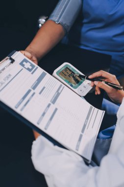 Hastanın tansiyonunu ölçen bir doktor. Hastanın kolunda tansiyon aleti var. Doktor da tansiyon monitörü kullanıyor..