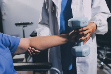 Evde dambıl kullanarak fizyoterapist eğitimi alan yaşlı bir kadın. Terapist, huzurevi egzersizlerinde yaşlı kadına yardım ediyor. Yaşlı bir hasta kollarını uzatmış halterler kullanıyor..