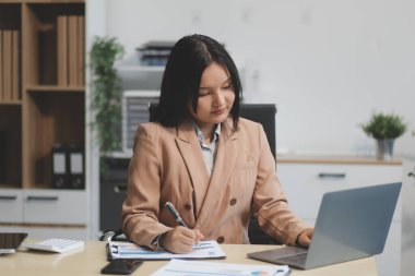Asyalı iş kadını dizüstü bilgisayar kullanıyor ve ofiste hesap makinesi ile çalışıyor, mali raporu, iş planı yatırımını, mali analiz konseptini analiz etmeyi planlıyor..