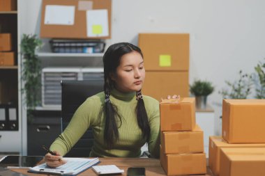 Girişim KOBİ küçük işletme girişimcisi önlük giyen Asyalı kadın dizüstü bilgisayar ve kutu kullanarak çevrimiçi müşterilere, çevrimiçi sme iş fikirlerine satış hazırlamak için siparişleri alır ve gözden geçirir.
