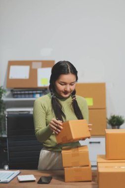 Girişim KOBİ küçük işletme girişimcisi önlük giyen Asyalı kadın dizüstü bilgisayar ve kutu kullanarak çevrimiçi müşterilere, çevrimiçi sme iş fikirlerine satış hazırlamak için siparişleri alır ve gözden geçirir.