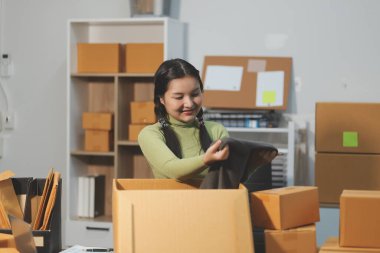 Girişim KOBİ küçük işletme girişimcisi önlük giyen Asyalı kadın dizüstü bilgisayar ve kutu kullanarak çevrimiçi müşterilere, çevrimiçi sme iş fikirlerine satış hazırlamak için siparişleri alır ve gözden geçirir.