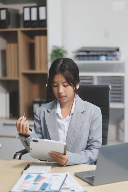 Başarılı Asyalı iş kadını dizüstü bilgisayarla gülümseyip ofisinde kahve fincanı tutuyor. Güvenilir Asyalı iş kadını ofiste mutlu mesut oturuyor..