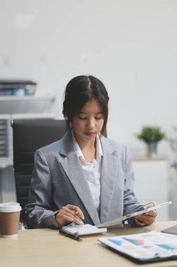 Başarılı Asyalı iş kadını dizüstü bilgisayarla gülümseyip ofisinde kahve fincanı tutuyor. Güvenilir Asyalı iş kadını ofiste mutlu mesut oturuyor..