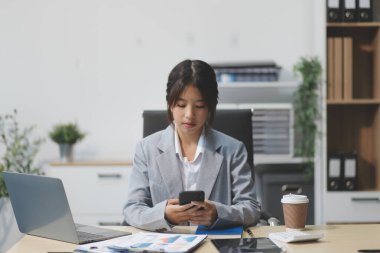 Ofisteki resmi takım elbiseli Asyalı iş kadını akıllı telefon ve çalışma süresince mutlu ve neşeli.