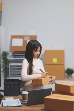 Girişim KOBİ küçük işletme girişimcisi önlük giyen Asyalı kadın dizüstü bilgisayar ve kutu kullanarak çevrimiçi müşterilere, çevrimiçi sme iş fikirlerine satış hazırlamak için siparişleri alır ve gözden geçirir.