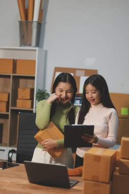 Girişim KOBİ küçük işletme girişimcisi önlük giyen Asyalı kadın dizüstü bilgisayar ve kutu kullanarak çevrimiçi müşterilere, çevrimiçi sme iş fikirlerine satış hazırlamak için siparişleri alır ve gözden geçirir.