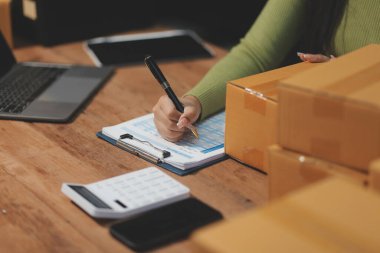 Girişim KOBİ küçük işletme girişimcisi önlük giyen Asyalı kadın dizüstü bilgisayar ve kutu kullanarak çevrimiçi müşterilere, çevrimiçi sme iş fikirlerine satış hazırlamak için siparişleri alır ve gözden geçirir.