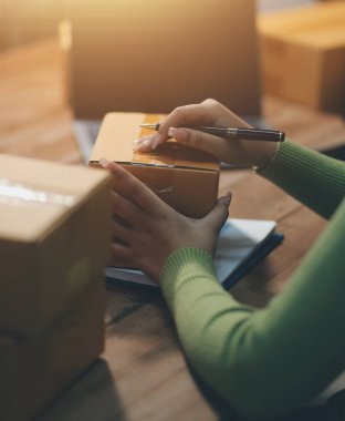 Girişim KOBİ küçük işletme girişimcisi önlük giyen Asyalı kadın dizüstü bilgisayar ve kutu kullanarak çevrimiçi müşterilere, çevrimiçi sme iş fikirlerine satış hazırlamak için siparişleri alır ve gözden geçirir.
