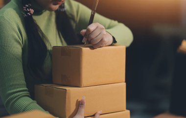 Girişim KOBİ küçük işletme girişimcisi önlük giyen Asyalı kadın dizüstü bilgisayar ve kutu kullanarak çevrimiçi müşterilere, çevrimiçi sme iş fikirlerine satış hazırlamak için siparişleri alır ve gözden geçirir.