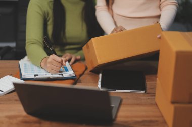 Girişim KOBİ küçük işletme girişimcisi önlük giyen Asyalı kadın dizüstü bilgisayar ve kutu kullanarak çevrimiçi müşterilere, çevrimiçi sme iş fikirlerine satış hazırlamak için siparişleri alır ve gözden geçirir.