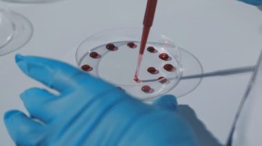 Bilim adamı elinde kırmızı sıvı bir pipet tutuyor.