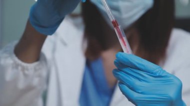 Koruyucu eldivenli bilim adamı elinde kanla tüp tutuyor.