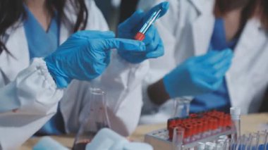 Koruyucu maskeli bilim adamı deney tüpünü sıvı ile tutuyor..