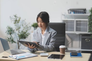 Başarılı Asyalı iş kadını dizüstü bilgisayarla gülümseyip ofisinde kahve fincanı tutuyor. Güvenilir Asyalı iş kadını ofiste mutlu mesut oturuyor..