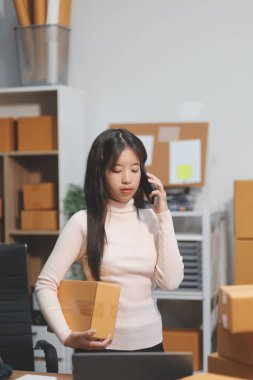 Girişim KOBİ küçük işletme girişimcisi önlük giyen Asyalı kadın dizüstü bilgisayar ve kutu kullanarak çevrimiçi müşterilere, çevrimiçi sme iş fikirlerine satış hazırlamak için siparişleri alır ve gözden geçirir.