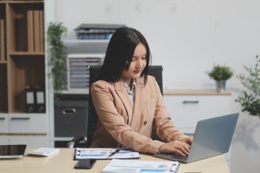 Asyalı iş kadını dizüstü bilgisayar kullanıyor ve ofiste hesap makinesi ile çalışıyor, mali raporu, iş planı yatırımını, mali analiz konseptini analiz etmeyi planlıyor..