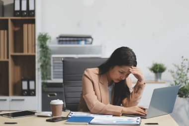 Yorgun ve Asyalı bir kadının portresi ofiste vergi bilgisayarıyla çalışıyor. Üzgün, mutsuz, endişeli, depresyon ya da çalışan hayatı stres konsepti