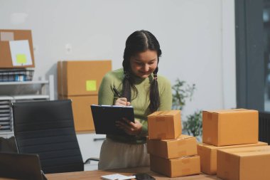 Girişim KOBİ küçük işletme girişimcisi önlük giyen Asyalı kadın dizüstü bilgisayar ve kutu kullanarak çevrimiçi müşterilere, çevrimiçi sme iş fikirlerine satış hazırlamak için siparişleri alır ve gözden geçirir.