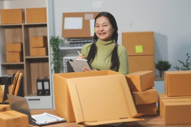 Girişim KOBİ küçük işletme girişimcisi önlük giyen Asyalı kadın dizüstü bilgisayar ve kutu kullanarak çevrimiçi müşterilere, çevrimiçi sme iş fikirlerine satış hazırlamak için siparişleri alır ve gözden geçirir.