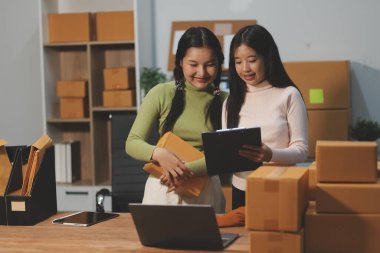 Girişim KOBİ küçük işletme girişimcisi önlük giyen Asyalı kadın dizüstü bilgisayar ve kutu kullanarak çevrimiçi müşterilere, çevrimiçi sme iş fikirlerine satış hazırlamak için siparişleri alır ve gözden geçirir.