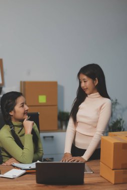 Girişim KOBİ küçük işletme girişimcisi önlük giyen Asyalı kadın dizüstü bilgisayar ve kutu kullanarak çevrimiçi müşterilere, çevrimiçi sme iş fikirlerine satış hazırlamak için siparişleri alır ve gözden geçirir.