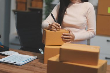 Girişim KOBİ küçük işletme girişimcisi önlük giyen Asyalı kadın dizüstü bilgisayar ve kutu kullanarak çevrimiçi müşterilere, çevrimiçi sme iş fikirlerine satış hazırlamak için siparişleri alır ve gözden geçirir.