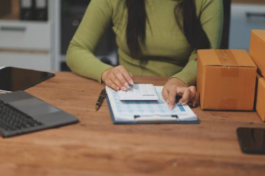 Girişim KOBİ küçük işletme girişimcisi önlük giyen Asyalı kadın dizüstü bilgisayar ve kutu kullanarak çevrimiçi müşterilere, çevrimiçi sme iş fikirlerine satış hazırlamak için siparişleri alır ve gözden geçirir.