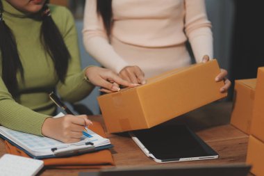 Girişim KOBİ küçük işletme girişimcisi önlük giyen Asyalı kadın dizüstü bilgisayar ve kutu kullanarak çevrimiçi müşterilere, çevrimiçi sme iş fikirlerine satış hazırlamak için siparişleri alır ve gözden geçirir.