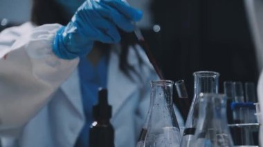 Koruyucu kıyafetli bilim adamı laboratuarda sıvı şişeyi tutuyor.