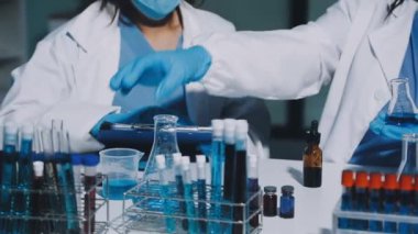 Koruyucu eldivenler giymiş bilim adamları ve test tüplerinde çalışan koruyucu maskeler.