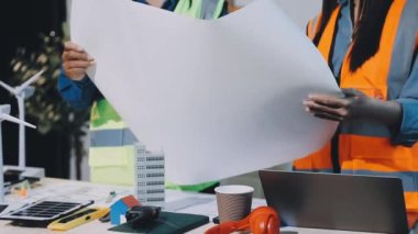 Ofiste dizüstü bilgisayar ve proje planları üzerinde çalışan mühendis.