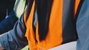 Elinde not panosu ve kalemle güvenlik ekipmanlarıyla çalışan kadın işçiler..