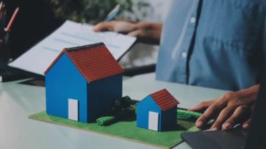 Emlakçı ev modelini tutuyor ve ev modelini gösteriyor.