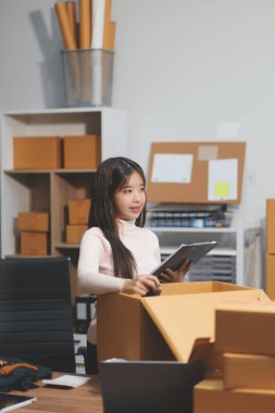 Girişim KOBİ küçük işletme girişimcisi önlük giyen Asyalı kadın dizüstü bilgisayar ve kutu kullanarak çevrimiçi müşterilere, çevrimiçi sme iş fikirlerine satış hazırlamak için siparişleri alır ve gözden geçirir.