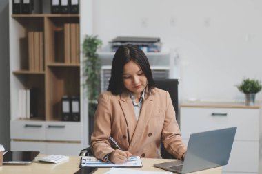 Asyalı iş kadını dizüstü bilgisayar kullanıyor ve ofiste hesap makinesi ile çalışıyor, mali raporu, iş planı yatırımını, mali analiz konseptini analiz etmeyi planlıyor..