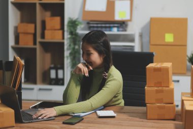 Girişim KOBİ küçük işletme girişimcisi önlük giyen Asyalı kadın dizüstü bilgisayar ve kutu kullanarak çevrimiçi müşterilere, çevrimiçi sme iş fikirlerine satış hazırlamak için siparişleri alır ve gözden geçirir.