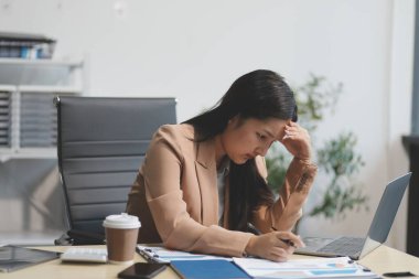 Yorgun ve Asyalı bir kadının portresi ofiste vergi bilgisayarıyla çalışıyor. Üzgün, mutsuz, endişeli, depresyon ya da çalışan hayatı stres konsepti