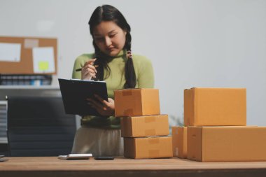 Girişim KOBİ küçük işletme girişimcisi önlük giyen Asyalı kadın dizüstü bilgisayar ve kutu kullanarak çevrimiçi müşterilere, çevrimiçi sme iş fikirlerine satış hazırlamak için siparişleri alır ve gözden geçirir.