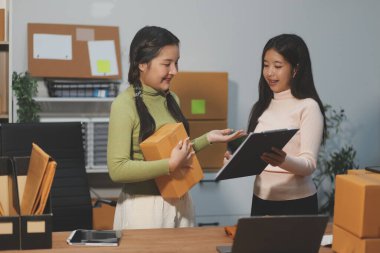 Girişim KOBİ küçük işletme girişimcisi önlük giyen Asyalı kadın dizüstü bilgisayar ve kutu kullanarak çevrimiçi müşterilere, çevrimiçi sme iş fikirlerine satış hazırlamak için siparişleri alır ve gözden geçirir.