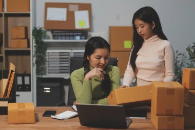 Girişim KOBİ küçük işletme girişimcisi önlük giyen Asyalı kadın dizüstü bilgisayar ve kutu kullanarak çevrimiçi müşterilere, çevrimiçi sme iş fikirlerine satış hazırlamak için siparişleri alır ve gözden geçirir.