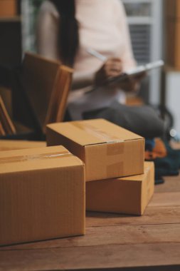 Girişim KOBİ küçük işletme girişimcisi önlük giyen Asyalı kadın dizüstü bilgisayar ve kutu kullanarak çevrimiçi müşterilere, çevrimiçi sme iş fikirlerine satış hazırlamak için siparişleri alır ve gözden geçirir.