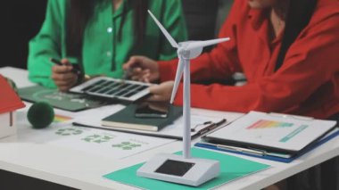 Gündelik giyimli genç Asyalı kadın dizüstü bilgisayarla çalışıyor ve elinde bir model ev tutuyor ve yeni bir ev için yeni bir proje yapmak için tablet kullanıyor..